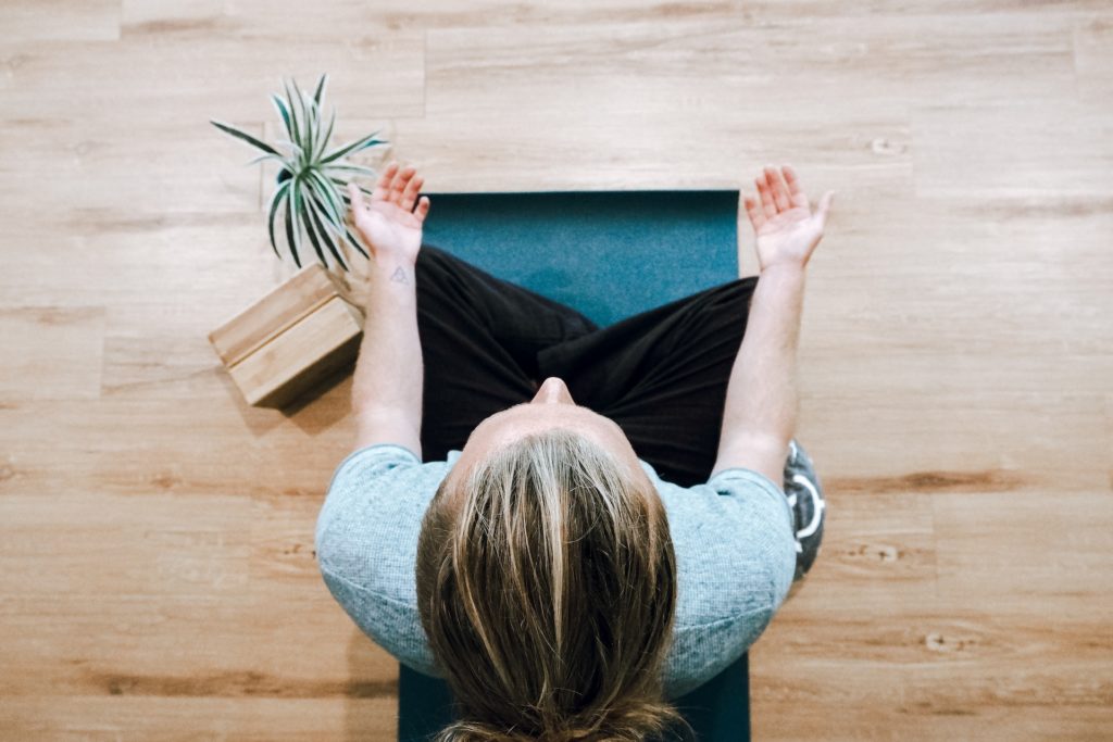 woman sitting cross-legged meditating on yoga mat with hands resting on knees and palms facing upwards