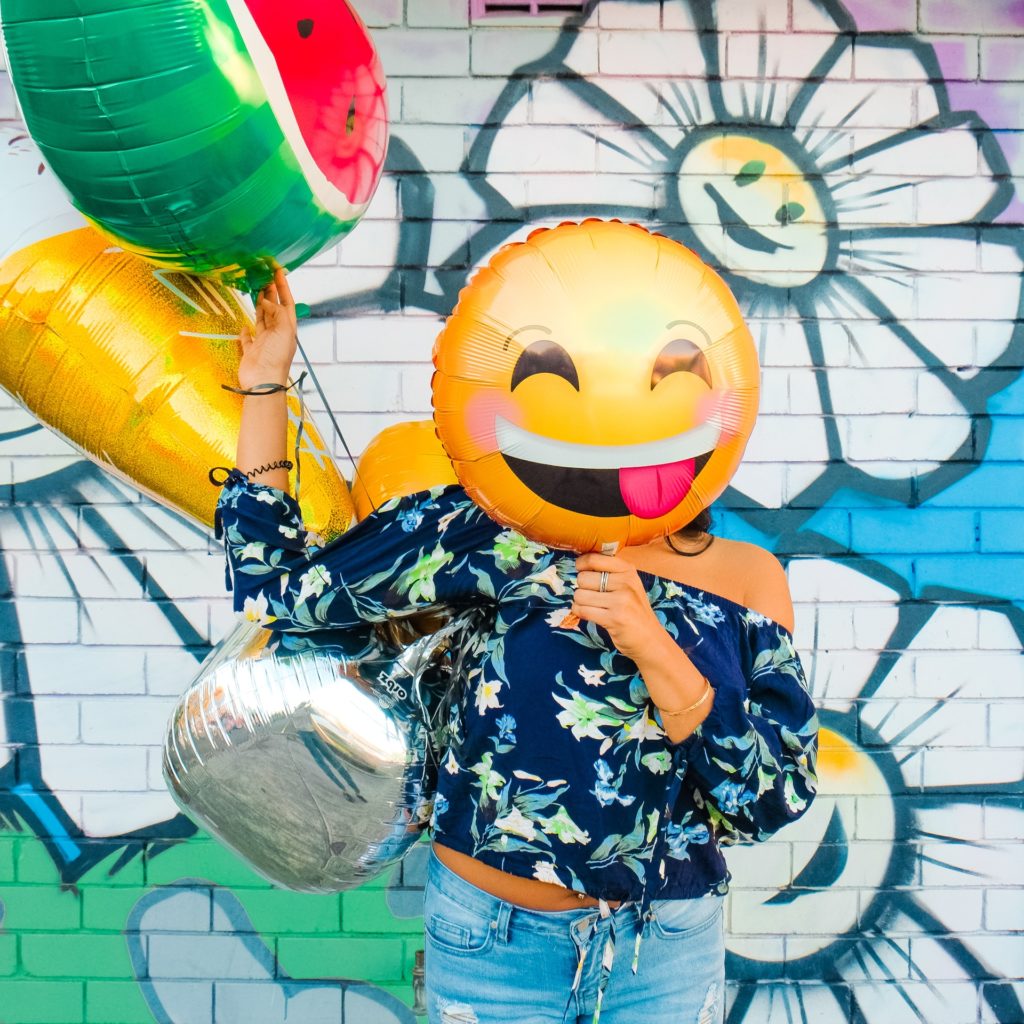 female with blue floral blouse holding a smiley face balloon in front of her face