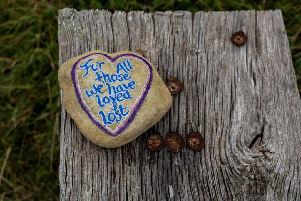 tree stump with painted rock that says,"for all those we have loved & lost""