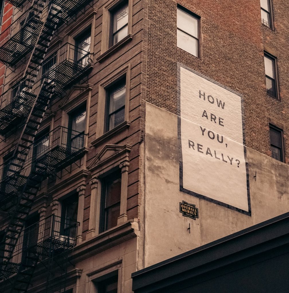 brown brick high rise building with fire escapes and a sign that says, "how are you, really?"